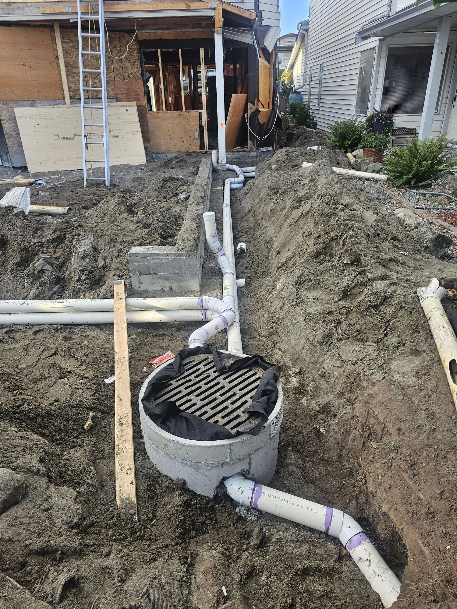 Perimeter drainage pipes and a concrete sump installed beside a residential foundation